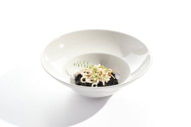 Mürekkep balıklı risotto. Siyah risotto tabağı beyaz arka planda izole. Kalamar halkalarıyla kaplı mürekkepli risotto. Beyaz arkaplan üzerinde gurme restoran yemeği