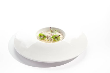 Beyaz restoran tabağında yengeç etli risotto. Parmesan peyniri ve yeşil yapraklarla süslenmiş. Beyaz arka planda izole edilmiş beyaz soslu lezzetli yengeç etli risotto. Deniz mahsullü pilav
