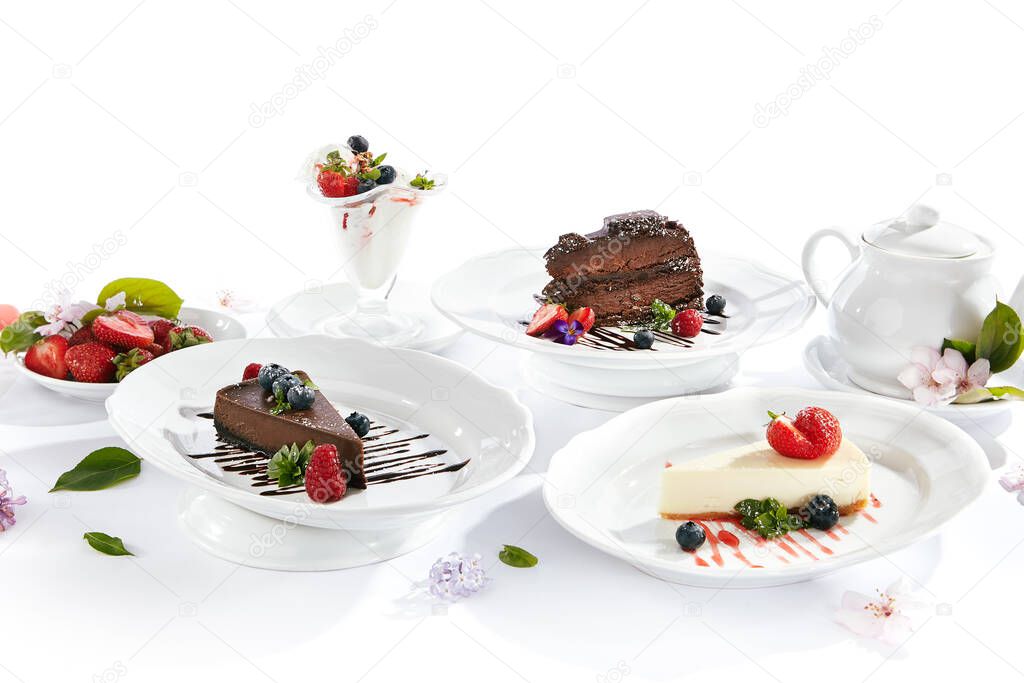 Dessert Table - created with Chocolate Cake, Classic Cheesecake, Ice Cream  and Chocolate Cheesecake. Fresh spring flowers on white table with berries and tea pot. Cake slice topped with berries and chocolate sauce