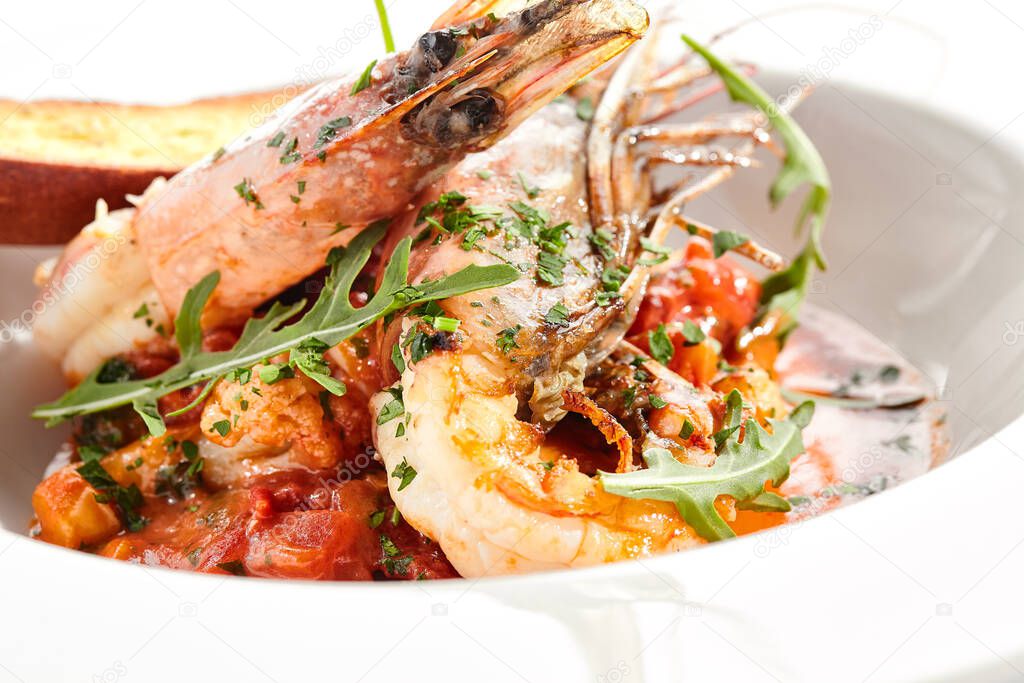 Seafood with tomato sauce on white restaurant plate. Shrimp seafood and tomato stew garnished with fried bread. Isolated on white background