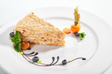 Bir parça Napolyon keki. Kremalı vanilyalı tatlı tabakta. Naneli ve yaban mersinli lezzetli hamur işi. Beyaz arka planda katmanlı fırında turta. Tatlı yemek sunumu