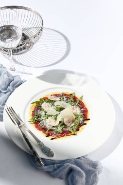 Mantarlı sığır carpaccio ve parmesan peyniri. Beyaz masa üzerinde sığır eti carpaccio ile süslü akşam yemeği ve basit çağdaş dekor. Güneş ışığı ve sert gölge, hayat devam ediyor. Et carpaccio aperatif
