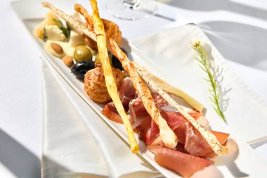 Şarap şişesi ve bardakla aperatif şarabı. Beyaz şarap ve abur cubur setiyle akşam yemeği. Basit çağdaş dekorlu beyaz masa. Güneş ışığı ve sert gölge, hayat devam ediyor. Şarap başlatıcı seti