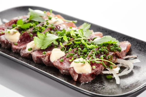 Beef tataki - seared beef,. thinly sliced sashimi style. Beef tataki served with delicious ponzu tataki sauce. Japanese style meat on black plate isolated on white background.