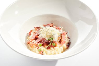 Beyaz restoran tabağında risotto alla carbonara. Pastırmalı ve yumurtalı risotto, mikro yeşilliklerle süslenmiş. Parmesan peynirli risotto.