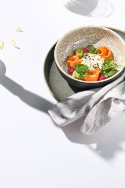 Somon, salatalık ve pancar ile ev yapımı peynir salatası. Beyaz masada somon salatasıyla akşam yemeği ve basit çağdaş dekorasyon. Güneş ışığı ve sert gölge, hayat devam ediyor. Somon salatası kasesi