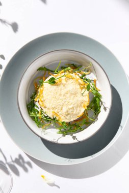 Peynir sosunun altında sığır etli tartar ve kızartılmış soğan. Beyaz masada sığır etli tartar ve çağdaş dekorasyonla süslü bir akşam yemeği. Güneş ışığı ve sert gölge, hayat devam ediyor. Sığır eti, mavi yemek.