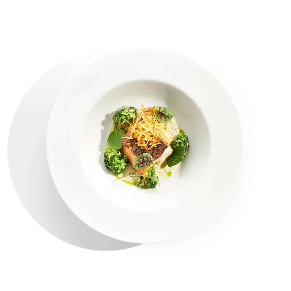 ブロッコリーとクリームソースと揚げ魚 緑色の葉を持つ健康的なローストタラ 白い背景に孤立した白いレストランプレート上の揚げ魚 — ストック写真
