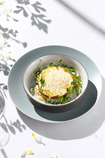 stock image Beef tartare under cheese sauce with deep fried onion. Fancy dinning with beef tartare on white table with simple contemporary decoration. Sunlight and harsh shadow still life. Beef tartare blue dish