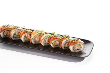 Uluslararası suşi rulosu üzerinde füme yılan balığı ve susam tohumu var. İçinde avokado ve yengeç eti olan suşi rulosu. Siyah tahta suşi tabağı beyaz arka planda izole edilmiş. Nefis suşi restoranı menüsü.
