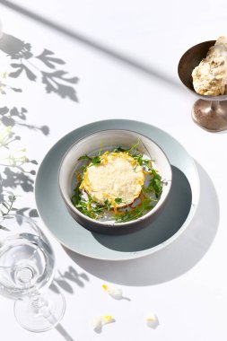 Peynir sosunun altında sığır etli tartar ve kızartılmış soğan. Beyaz masada sığır etli tartar ve çağdaş dekorasyonla süslü bir akşam yemeği. Güneş ışığı ve sert gölge, hayat devam ediyor. Sığır eti, mavi yemek.