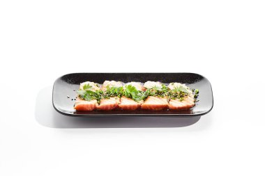 Somon tataki - kavrulmuş somon balığı, ince dilimlenmiş saşimi usulü. Lezzetli turunç ponzu tataki sosu ve taze yeşilliklerle servis edilen somon tataki. Siyah tabakta Japon deniz ürünleri beyaz arka planda izole edilmiştir.