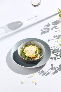 Peynir sosunun altında sığır etli tartar ve kızartılmış soğan. Beyaz masada sığır etli tartar ve çağdaş dekorasyonla süslü bir akşam yemeği. Güneş ışığı ve sert gölge, hayat devam ediyor. Sığır eti, mavi yemek.