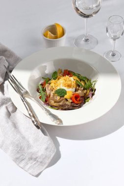 Yabanturpu soslu sığır dili salatası sosu ve taze yeşil yapraklar. Cam kaplı beyaz masa üzerinde gümüş çatal bıçak takımı olan beyaz bir restoran tabağı. Sebzeli et kasesi. Salata lokantası