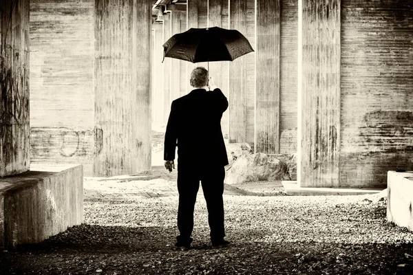 Artistic creative image of unrecognizable man in suit holding a umbrella in a concrete environment.