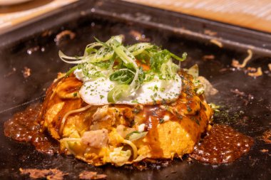 Okonomiyaki cızırdayan bir tavada. Okonomiyaki, lahana, yumurta ve et ya da deniz ürünleri gibi diğer malzemelerle karıştırılmış un hamurundan yapılan lezzetli bir Japon gözlemesidir.