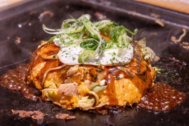 Okonomiyaki cızırdayan bir tavada. Okonomiyaki, lahana, yumurta ve et ya da deniz ürünleri gibi diğer malzemelerle karıştırılmış un hamurundan yapılan lezzetli bir Japon gözlemesidir.