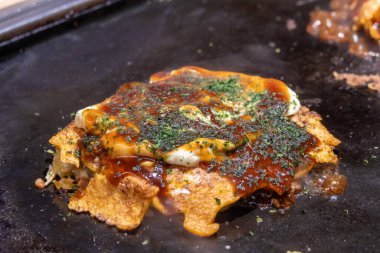 Okonomiyaki cızırdayan bir tavada. Okonomiyaki, lahana, yumurta ve et ya da deniz ürünleri gibi diğer malzemelerle karıştırılmış un hamurundan yapılan lezzetli bir Japon gözlemesidir.