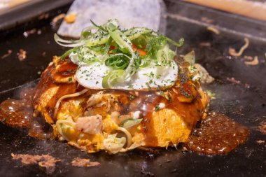 Okonomiyaki cızırdayan bir tavada. Okonomiyaki, lahana, yumurta ve et ya da deniz ürünleri gibi diğer malzemelerle karıştırılmış un hamurundan yapılan lezzetli bir Japon gözlemesidir.
