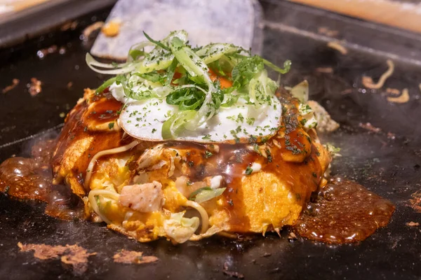 Okonomiyaki cızırdayan bir tavada. Okonomiyaki, lahana, yumurta ve et ya da deniz ürünleri gibi diğer malzemelerle karıştırılmış un hamurundan yapılan lezzetli bir Japon gözlemesidir.