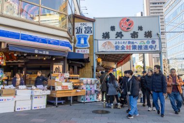 Tokyo, Japonya-28 Aralık 2025: Tokyo 'daki Tsukiji Dış Pazarı' nı ziyaret eden turistler. Pazar, özellikle deniz ürünleri aşıkları olmak üzere aşçılık deneyimleri arayan ziyaretçiler için hareketli bir merkez olmaya devam ediyor.