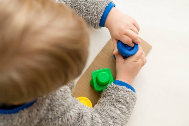 Şekiller, renkler ve ince motor beceriler. Yeni yürümeye başlayan çocuk cıvatanın fındığını çeviriyor. Eşleşen iplikte doğru renk bölümünü bükme görevi.