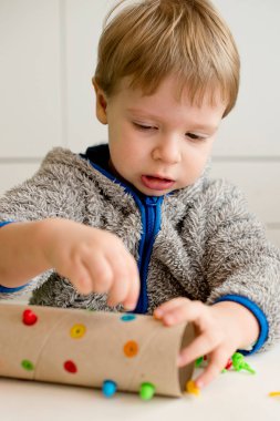 bir renge uyuyor. Atanan deliğe doğru renk iğnesi yerleştir. Konsantre bebek yüzü, yeni bir görev üzerinde çalışıyor. Bebek elleri kağıt tüpte. iyi motor becerileri, Montessori, ergotherapy, DIY