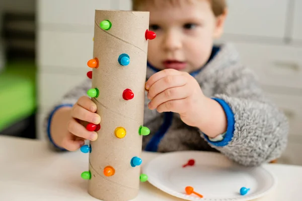 bir renge uyuyor. Atanan deliğe doğru renk iğnesi yerleştir. Konsantre bebek yüzü, yeni bir görev üzerinde çalışıyor. Bebek elleri kağıt tüpte. iyi motor becerileri, Montessori, ergotherapy, DIY