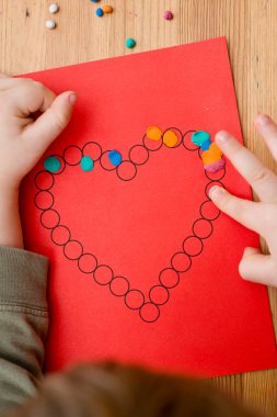 Annem için sevgililer günü tebrik kartı hazırlıyorum. Küçük çocuk baskılı kağıt kalbe hamur uyguluyor. Güzel motor beceriler, parmak koordinasyonu. bebekler için erken eğitim
