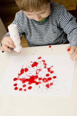 Güzel motor beceriler, el koordinasyonu. Küçük çocuk kalp iziyle kağıda pul yapıştırıyor. Sevgililer Günü teması.