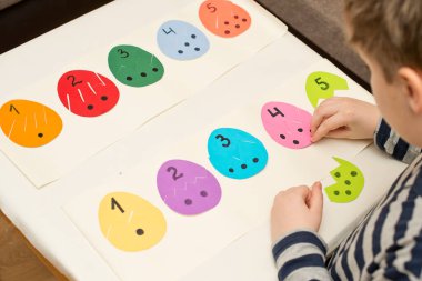 Farklı renkte kağıttan yumurtalar, bir tarafında sayılar, diğer tarafında da eşit miktarda noktalar var. Paskalya temalı oyun, figürün diğer tarafını bul.