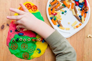 Paskalya konsepti. Çocuk renkli erişteleri yumurta şeklindeki plastiğin üzerine yerleştiriyor. Çocuklar ev fikirleri için oyuncak, çocuk istihdam, iyi motor beceriler, ergoterapi, duyusal terapi