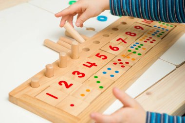 Çocuk farklı renkte ahşap halkalarla oynuyor. Sıralama, iyi motor beceriler, eğitim ve beyin egzersizi için terapi görevi. Matematik oyunu da dahil. Montessori tipi uygulama. Tahta oyuncaklar.