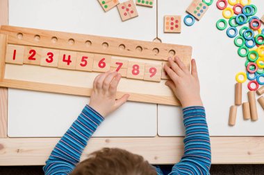 Çocuk farklı renkte ahşap halkalarla oynuyor. Sıralama, iyi motor beceriler, eğitim ve beyin egzersizi için terapi görevi. Matematik oyunu da dahil. Montessori tipi uygulama. Tahta oyuncaklar.