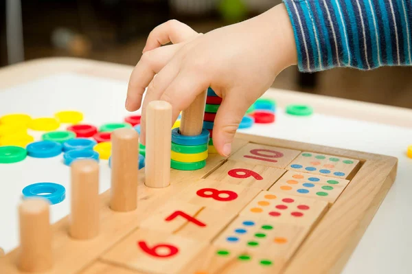 Çocuk farklı renkte ahşap halkalarla oynuyor. Sıralama, iyi motor beceriler, eğitim ve beyin egzersizi için terapi görevi. Matematik oyunu da dahil. Montessori tipi uygulama. Tahta oyuncaklar.