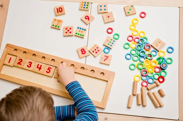 Çocuk farklı renkte ahşap halkalarla oynuyor. Sıralama, iyi motor beceriler, eğitim ve beyin egzersizi için terapi görevi. Matematik oyunu da dahil. Montessori tipi uygulama. Tahta oyuncaklar.
