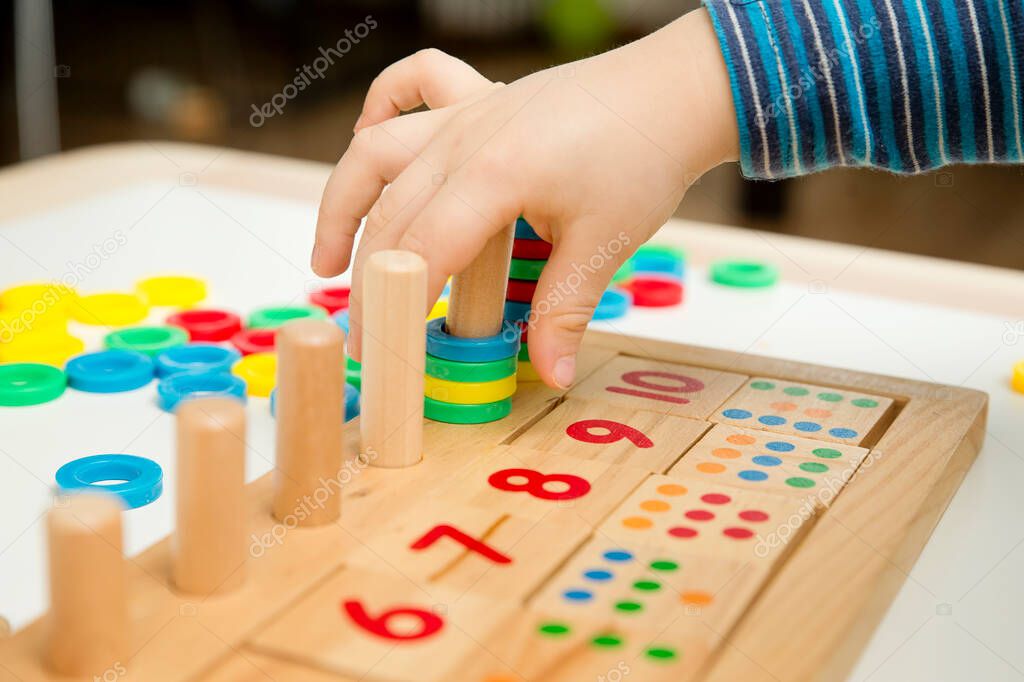Child playing with different color wooden rings. Sequence, fine motor skills, therapy task for education and brain exercise. Counting math play game.  Montessori type implement. Wooden toys.