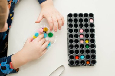 Duyusal alet. Çocuk beher tutacağına pompon yerleştiriyor.