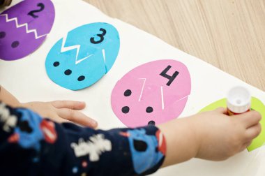 Beyaz masada farklı renkte kağıt yumurtalar. Paskalya temalı oyun, figürün diğer tarafını bul.