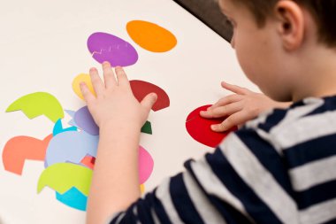 Beyaz masada farklı renkte kağıt yumurtalar. Paskalya temalı oyun, figürün diğer tarafını bul.