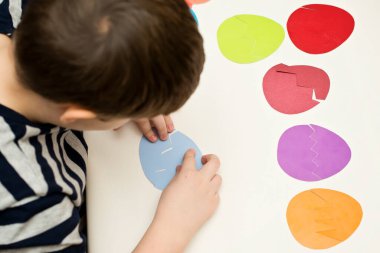 Beyaz masada farklı renkte kağıt yumurtalar. Paskalya temalı oyun, figürün diğer tarafını bul.