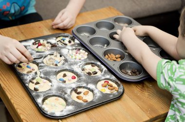 Cupcake 'i dekore eden çocuk. Pişirme formundan şeker, fındık ve süslemeler alıyor. Çocuklarla evde yemek pişirmek. Pasta dekorasyonu için bedava fikirler.