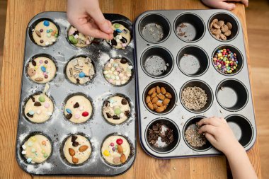 Cupcake 'i dekore eden çocuk. Pişirme formundan şeker, fındık ve süslemeler alıyor. Çocuklarla evde yemek pişirmek. Pasta dekorasyonu için bedava fikirler.