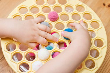 3 yaşında bir çocuk deliğe ponponları sokarak Rus köfte makinesiyle oynuyor. Plastik sepette renkli iplik topları