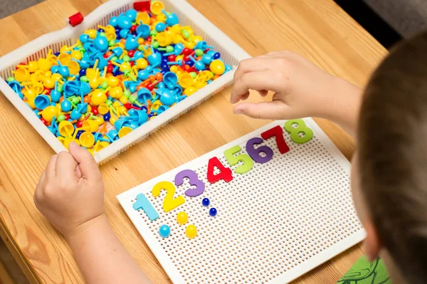By provided numbers boy inserting pins. Play at home. Implement for children to develop fine motoric skills, logical thinking through play. Learn counting and stimulate imagination, creativity.