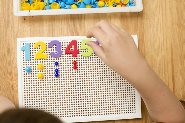 By provided numbers boy inserting pins. Play at home. Implement for children to develop fine motoric skills, logical thinking through play. Learn counting and stimulate imagination, creativity.