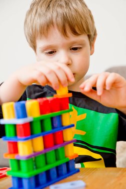 3 yaşındaki çocuk Numicon 'la oynuyor. Öğrenme araçları. Evde ders çalışıyor. Okul öncesi eğitim. Genç bilim adamı. Küçük dahi. Çocuk şekil ve figürlerle oynayarak matematik öğreniyor. Kaşifler bakar.