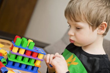 3 yaşındaki çocuk Numicon 'la oynuyor. Öğrenme araçları. Evde ders çalışıyor. Okul öncesi eğitim. Genç bilim adamı. Küçük dahi. Çocuk şekil ve figürlerle oynayarak matematik öğreniyor. Kaşifler bakar.