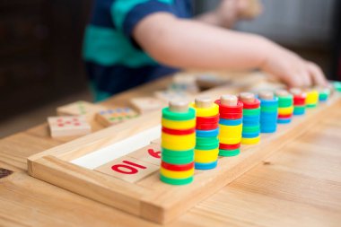 Çocuk farklı renkte ahşap halkalarla oynuyor. Sıralama, iyi motor beceriler, eğitim ve beyin egzersizi için terapi görevi. Matematik oyunu da dahil. Montessori tipi uygulama. Tahta oyuncaklar.