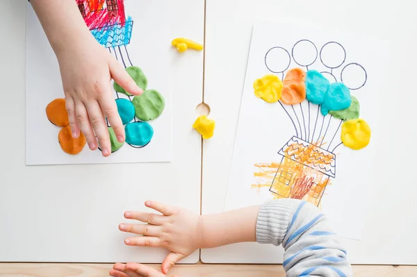 Two pairs of children hands coloring drawing of house with balloons with colored wax crayons. exercise for hand-eye coordination, stimulate imagination, creativity, develop fine motoric skills.